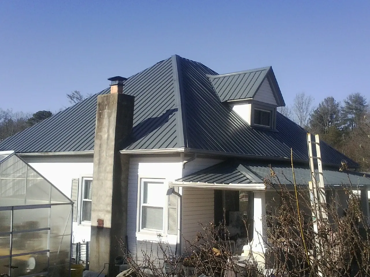 Dark blue standing seam metal roof on a white farmhouse with dormer — Slate & Tile Roof Repair by Roofing Brothers in Coppell