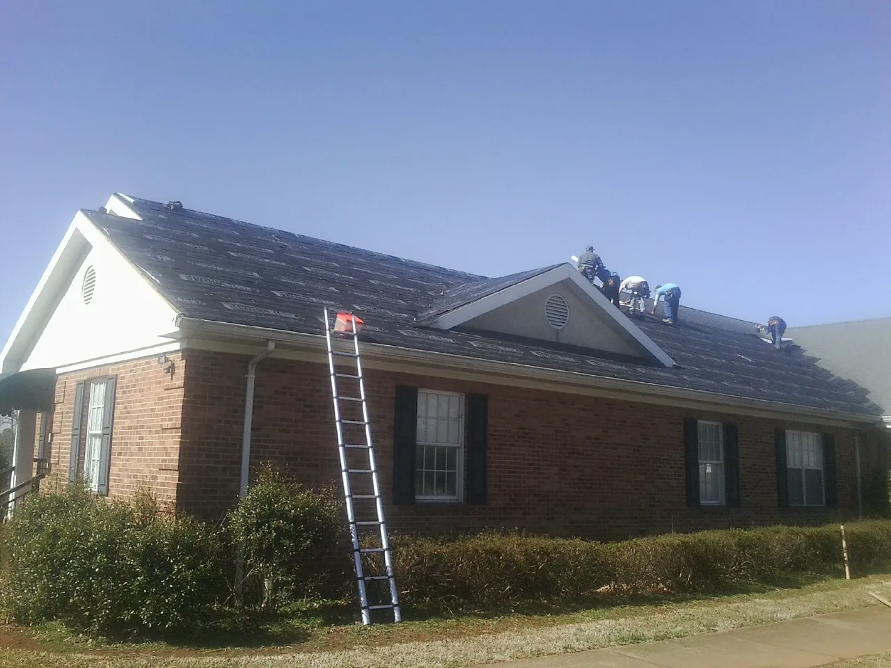 Crew tearing shingles off a brick ranch roof with a ladder set — Emergency Roof Repair work by our crew in Coppell