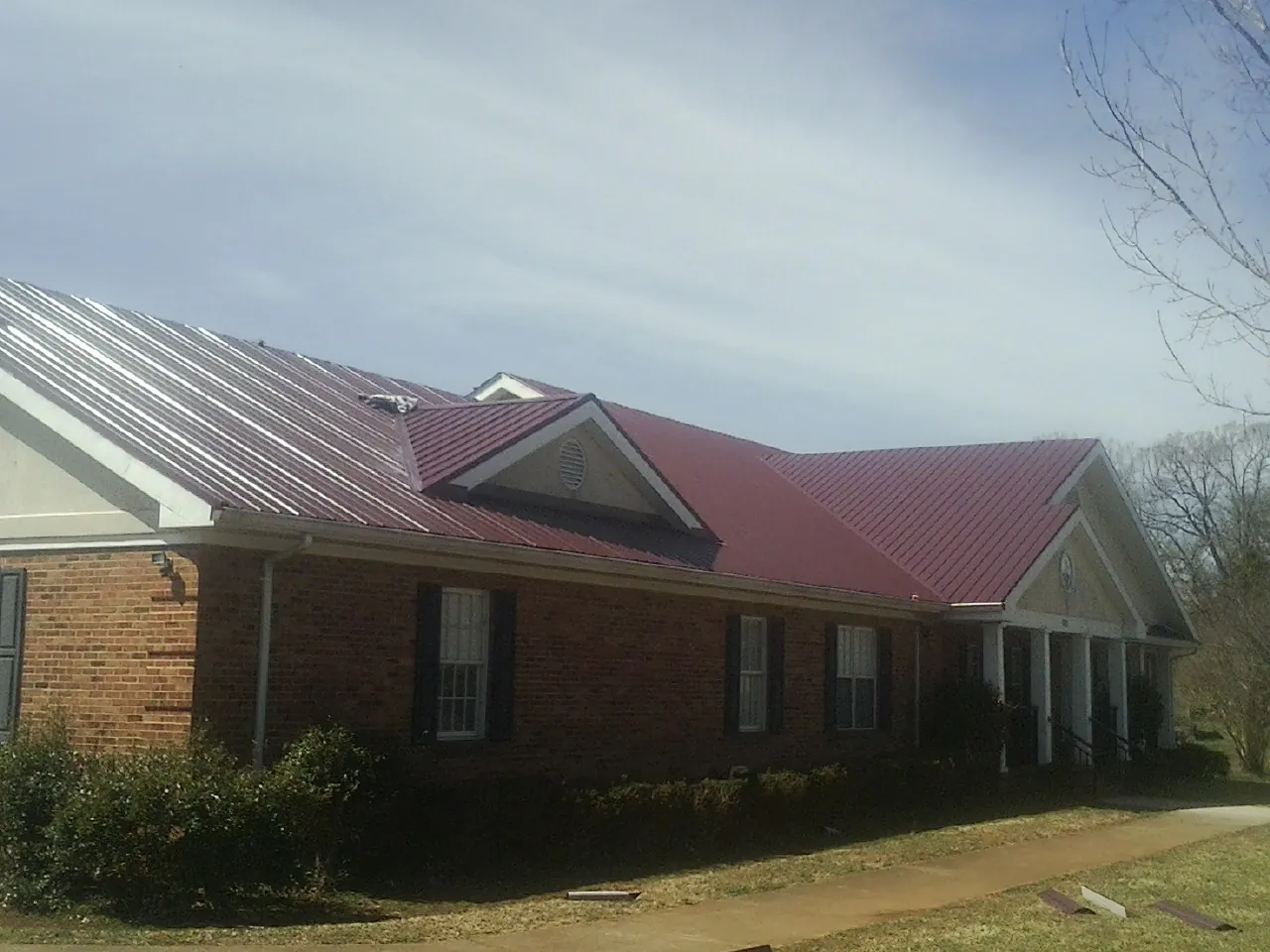Red metal roof with gabled entries on a long brick building, from a Hail Damage Roof Repair job in Coppell