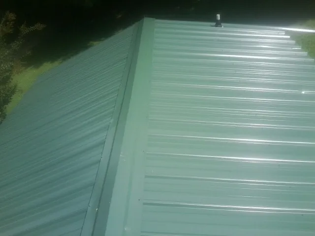 New green metal panels meeting at the ridge of a roof — Flat Roof Repair work by our crew in Coppell