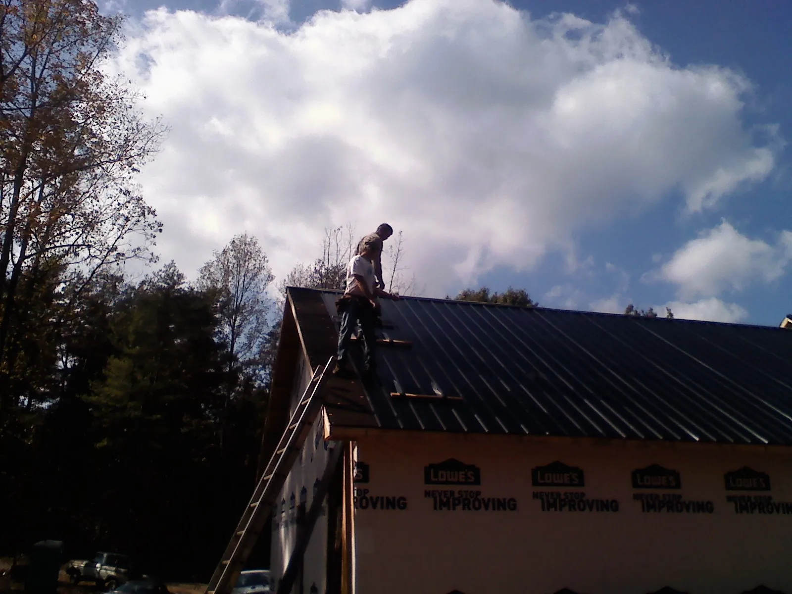 Roofer fastening dark metal panels high against a cloudy sky, from a Roof Inspection job in Coppell